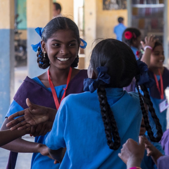 Sandhya, age 13, in a blue school uniform, excitedly talks with another schoolgirl.