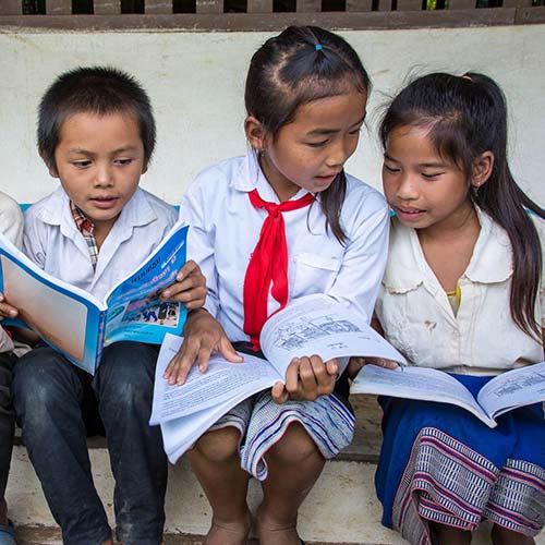 4 children from Laos sit on a step reading books together. 