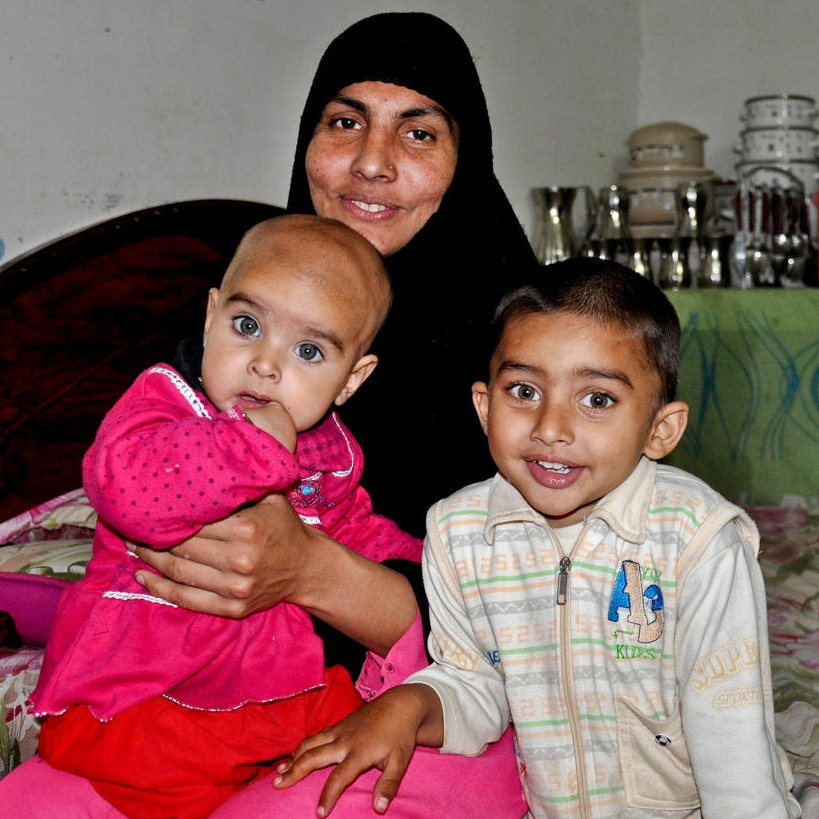 Mother Sobia smiles while sitting with her children Fatima, age 9 months, and Abdullah, age 3, inside their home in Pakistan.