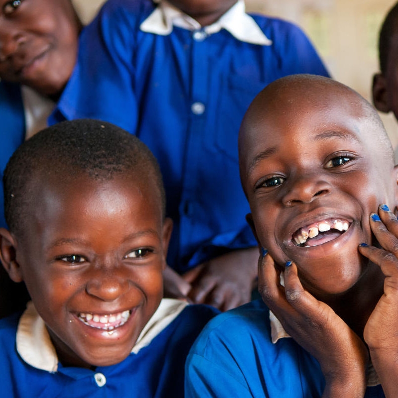 Young children wearing blue school uniforms share a laugh.