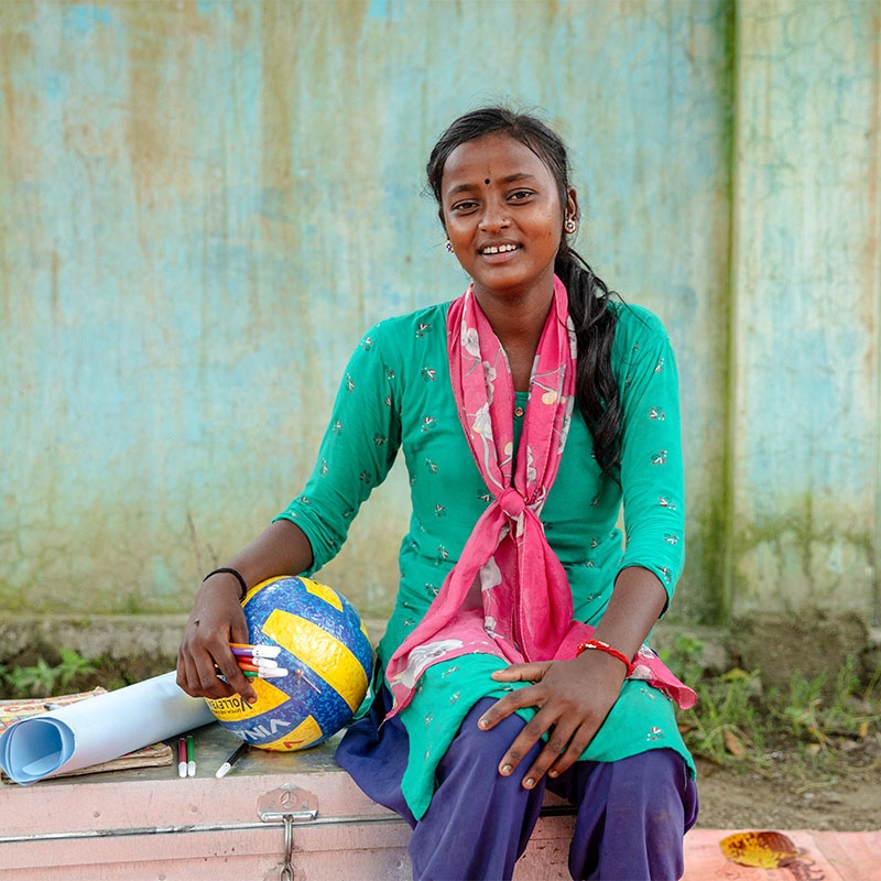 A teenage girl in Nepal sits with a soccer ball