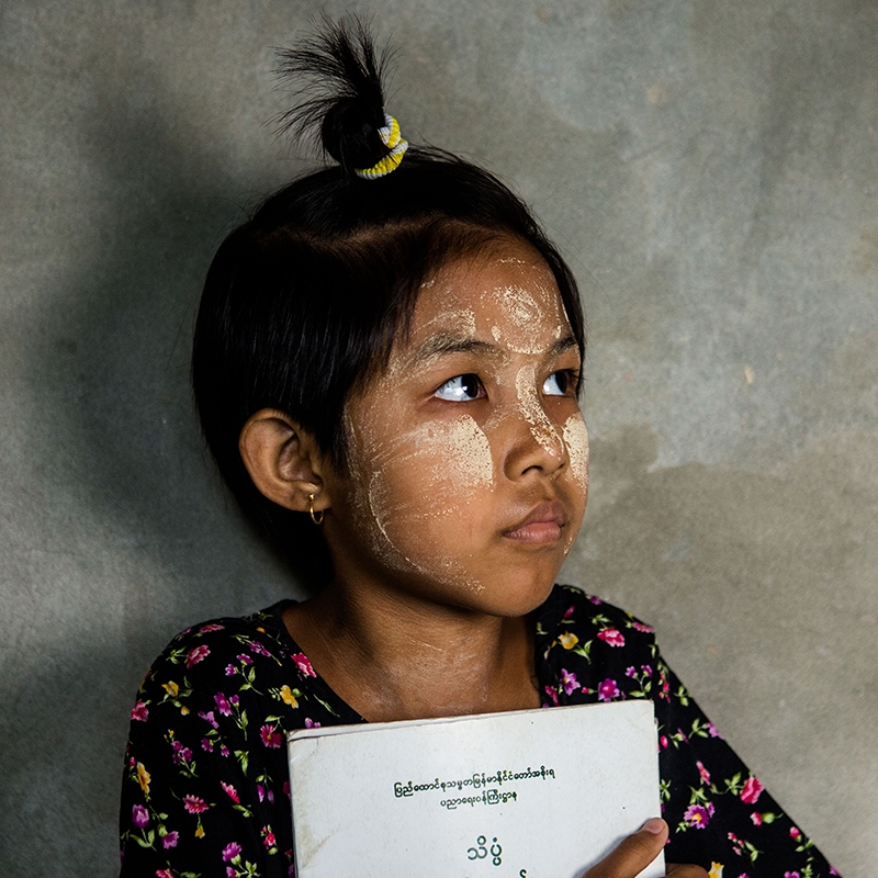 A young girl holding a book looking off into the distance. 