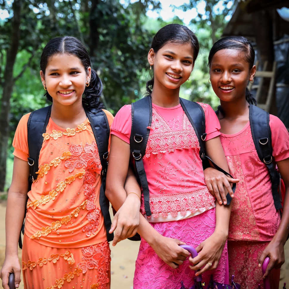 3 school girls wearing backpacks smiling at the camera