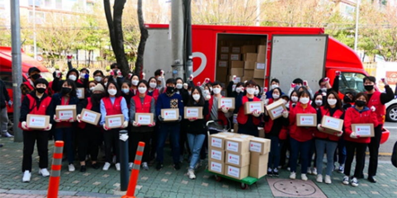 A group of volunteers in red vests hold cardboard boxes with Save the Children logos and stand in front of a red van. 