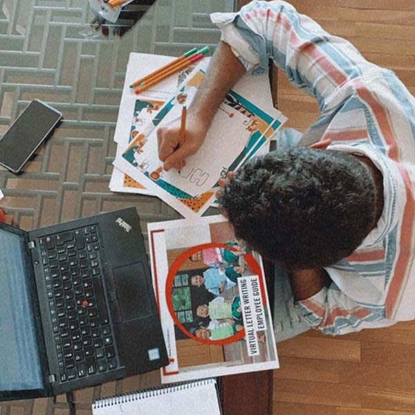 Overhead shot of a child at a laptop writing on a piece of paper.