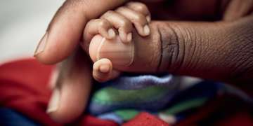 A baby’s tiny hand is wrapped around his mother’s thumb. The baby was born a twin and born prematurely – at 7 months – with a birthweight of 1.13 and .95kgs each. The mother is being taught Kangaroo Mother Care, a lifesaving technique that encourages skin-to-skin contact and breastfeeding for premature babies. Photo credit: Juozas Cernius/Save the Children, March 2018.