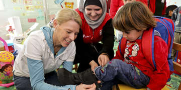Carolyn Miles, CEO and president of Save the Children helps a child in one of our child-friendly spaces put on a new pair of boots donated by TOMS at Za’atari refugee camp, Jordan. Photo Credit: Save the Children/Suzanna Klaucke 2014.