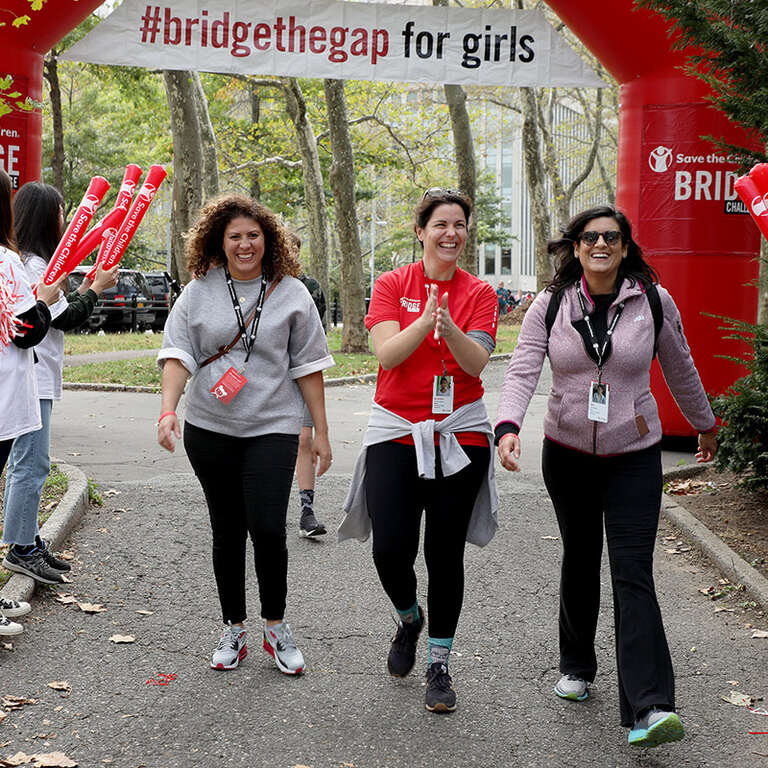Three women in Save the Children shirts cross the finish line during the Bridge the Gap Challenge in New York City.