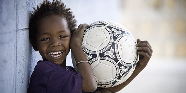 A boy in Ethipioa holds a soccer ball and smiles.