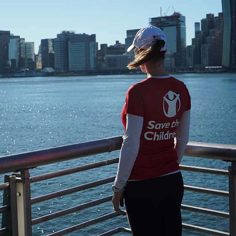A woman in a Save the Children shirt looks over the water. 