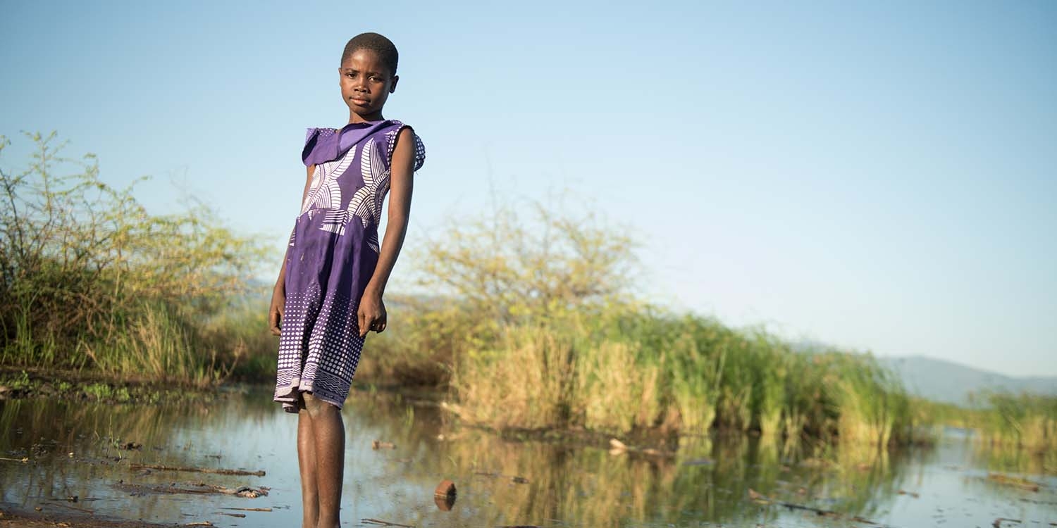 Malawi, a little girl in a purple dress on a boat, smiles at the camera