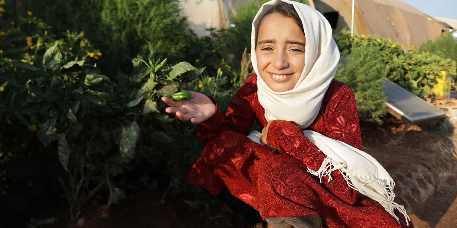 Syria, a little girl kneels showing off vegetables she's grown
