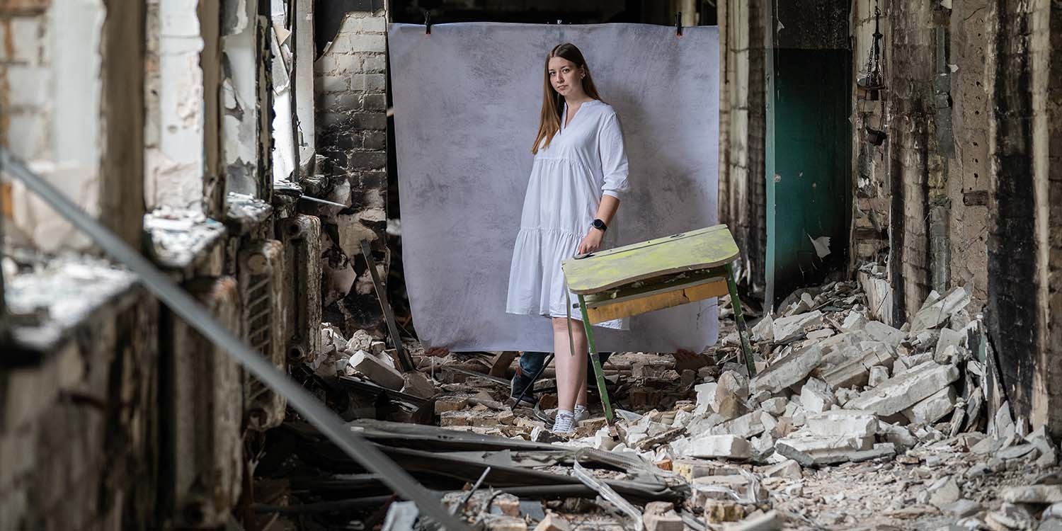 Ukraine, a teenage girl stands in the rubble of what used to be her school.
