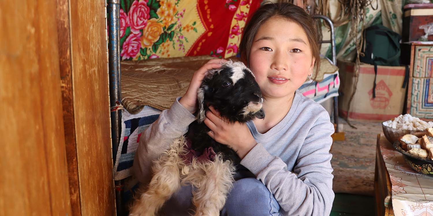 Mongolia, a little girl sits with her pet lamb.