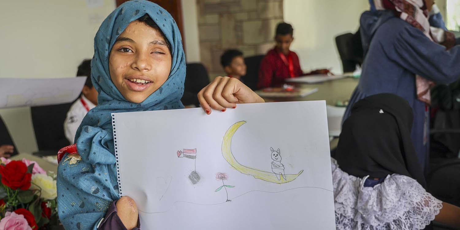 Yemen, a little girl who was injured by a landmine holds up a drawing.