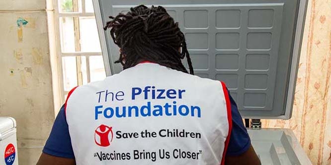 A Save the Children volunteer wears a vest with a corporate logo on the back. 