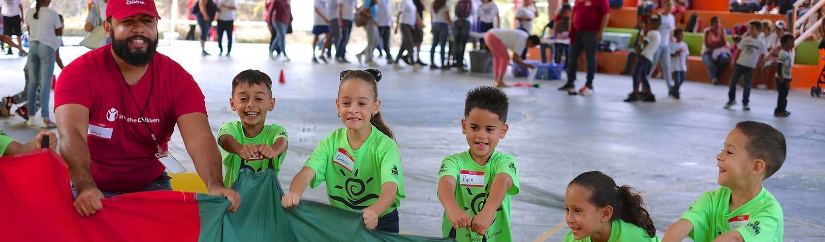 A group of children and Save the Children worker participate in Journey of Hope at the Mulitas Community Center in Puerto Rico, using the parachute to communicate their feelings following Hurricane Maria.