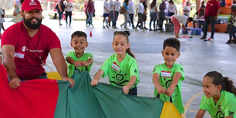 A group of children along with a Save the Children worker participate in Journey of Hope at the Mulitas Community Center in Puerto Rico, using the parachute to communicate their feelings following Hurricane Maria.