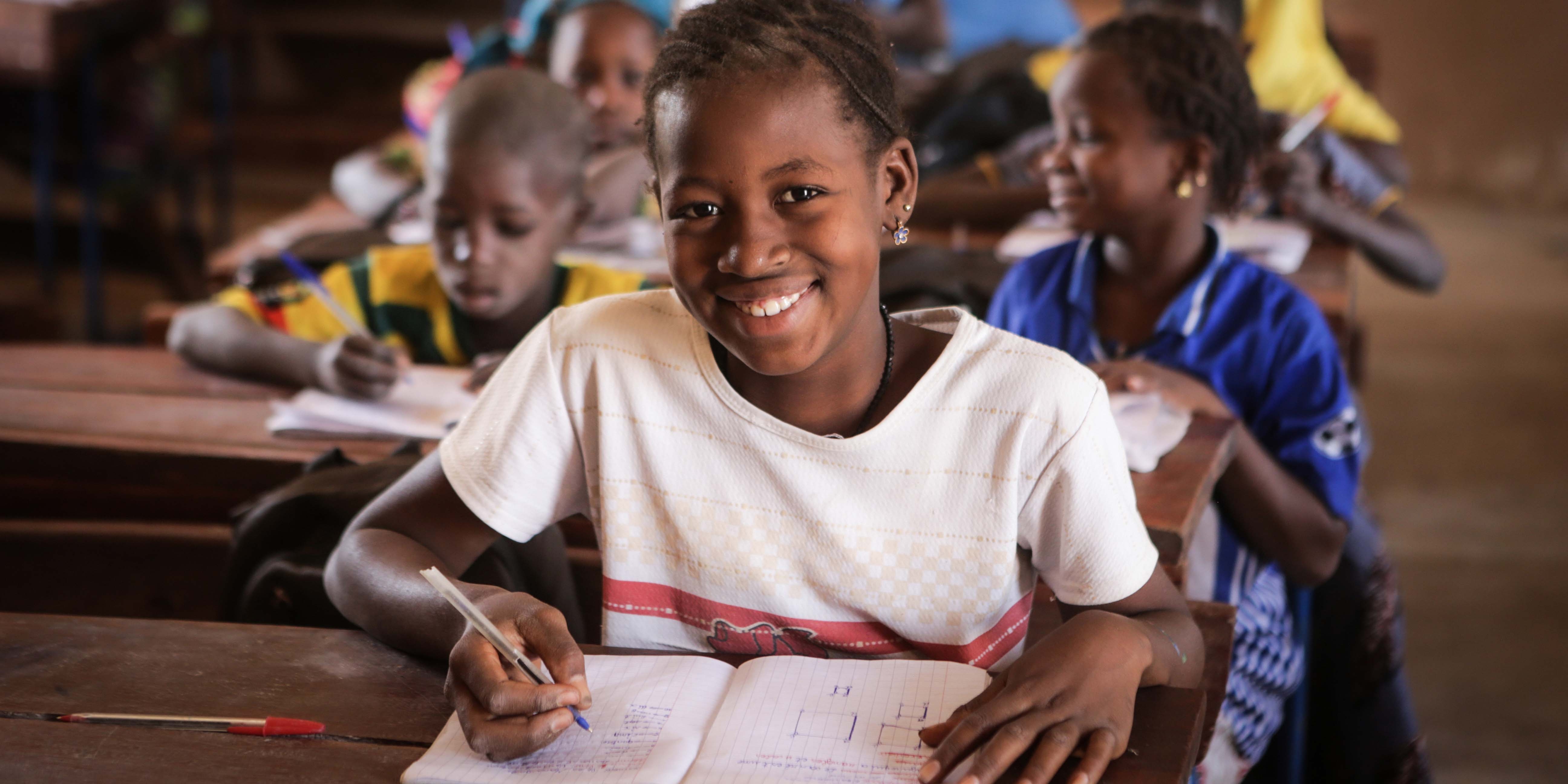 A school-age girl from Mali looks at camera while doing school work