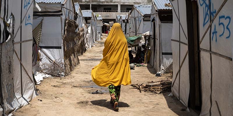 Nigeria, girl in yellow walks away from the camera through a refugee displacement camp