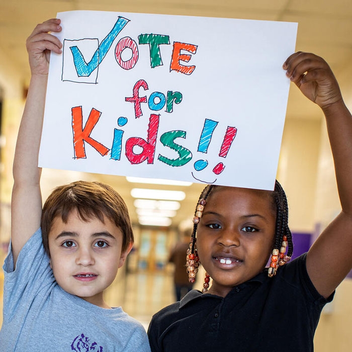 Two children hold a sign to "Vote for Kids."