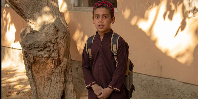 A boy wearing a backpack looks at the camera.