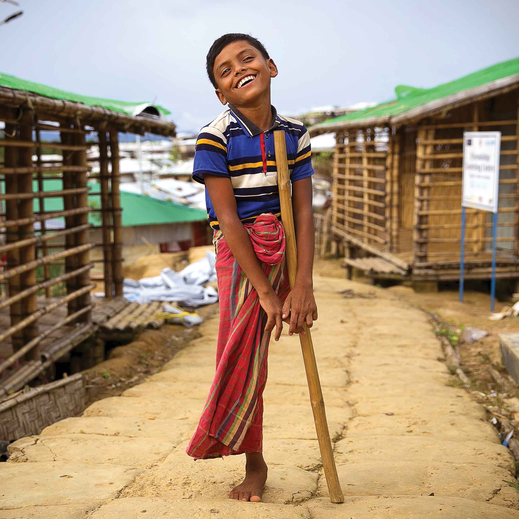 A boy stands and smiles while standing on one leg in Cox's Bazar, Bangladesh.