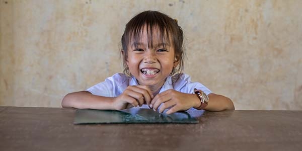 A young girl poses with a big smile on her face while sitting at a table in Cambodia.