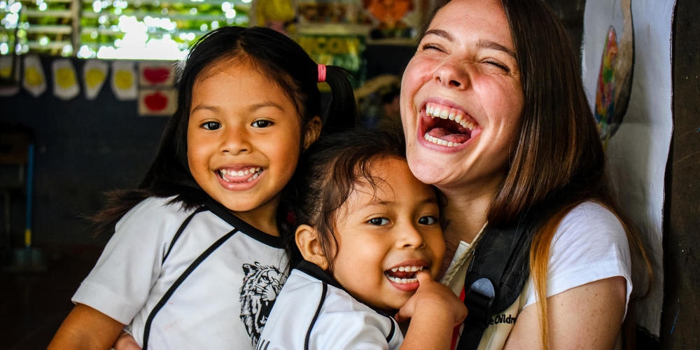 4-year-olds Julisa, left, and Valentina, center, embrace Save the Children staff member Victoria Zeger during a reading club for kindergarden students in the Sonsonate region of El Salvador. Photo credit: Save the Children, July 2018