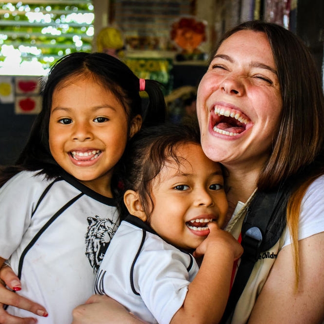 4-year-olds Julisa, left, and Valentina, center, embrace Save the Children staff member Victoria Zeger during a reading club for kindergarden students in the Sonsonate region of El Salvador. Photo Credit: Save the Children, July 2018 Victoria.