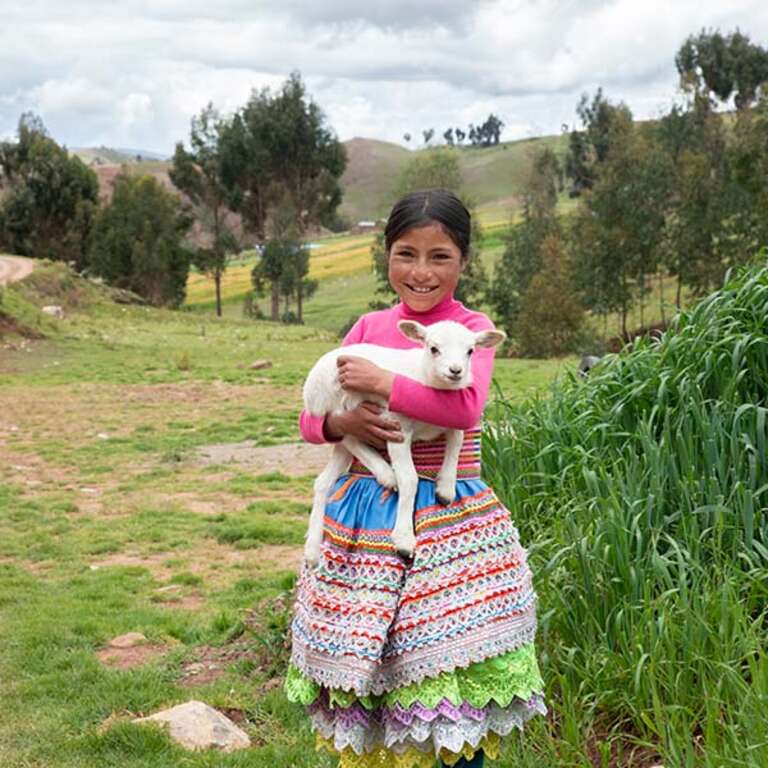 A young girl smiles while holding a baby goat in her arms. 