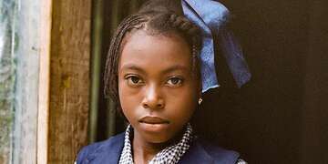 In Haiti, a girl wears a blue school uniform while standing in a doorway.