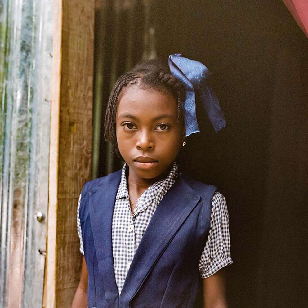 In Haiti, a girl wears a blue school uniform while holding a firm expression. 