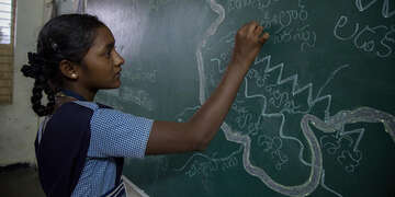 A girl from India stands in front of a chalk board