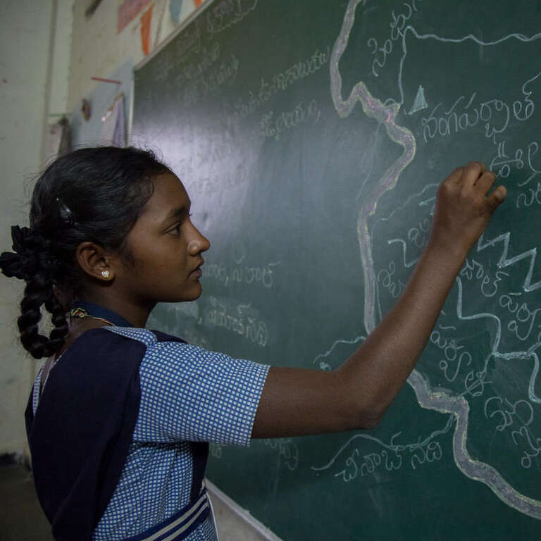 A girl in a blue and white dress writes on a chalkboard.