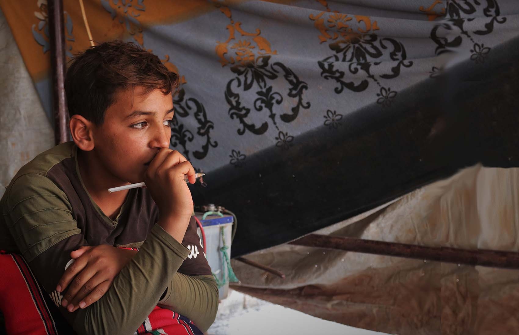 A 12-year old boy uses a cell phone to continue studying outside of school while resting at his home in a refugee camp in Syria.