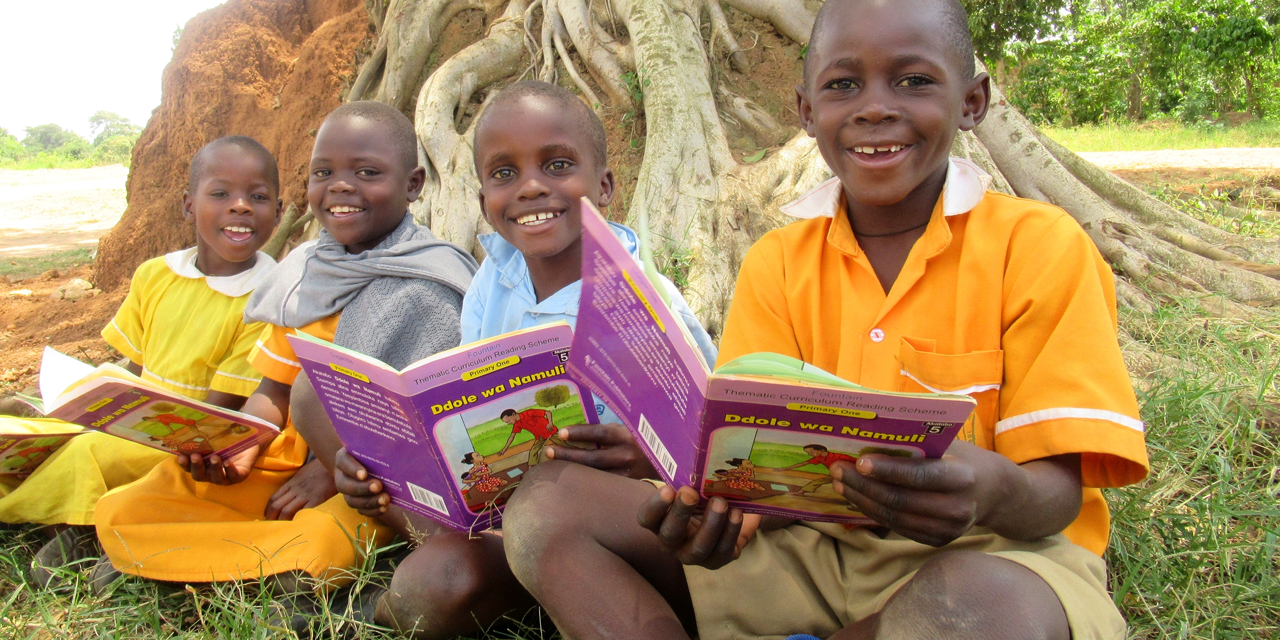 Four children sitting on the ground, holding books and smiling. 