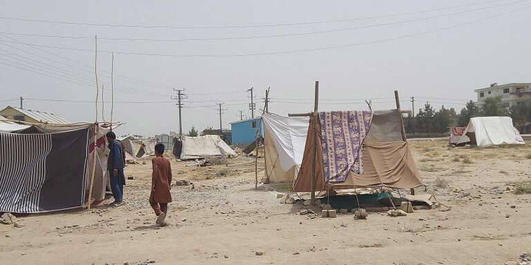 A boy walks with his back to the camera through a refugee camp. 