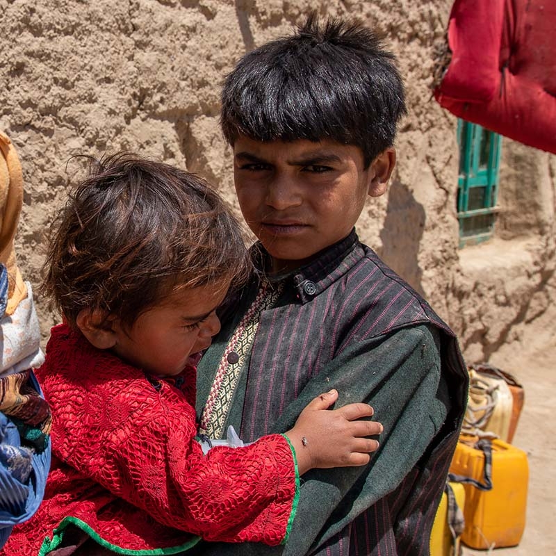 In Afghanistan, a boy holds his younger sibling outside the family's home.