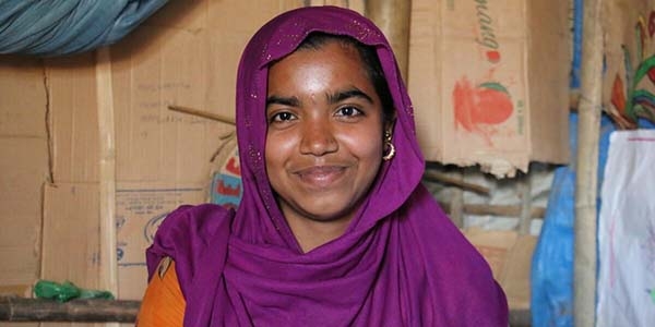 A teenage girl in a purple head scarf smiles and looks into the camera.