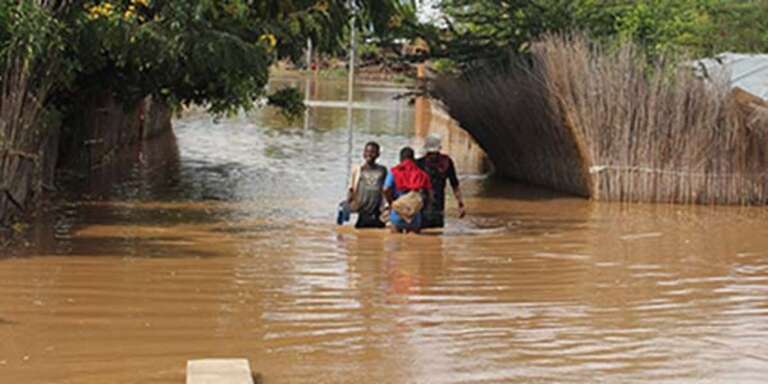 Three people walk through a flooded village in Burundi. 