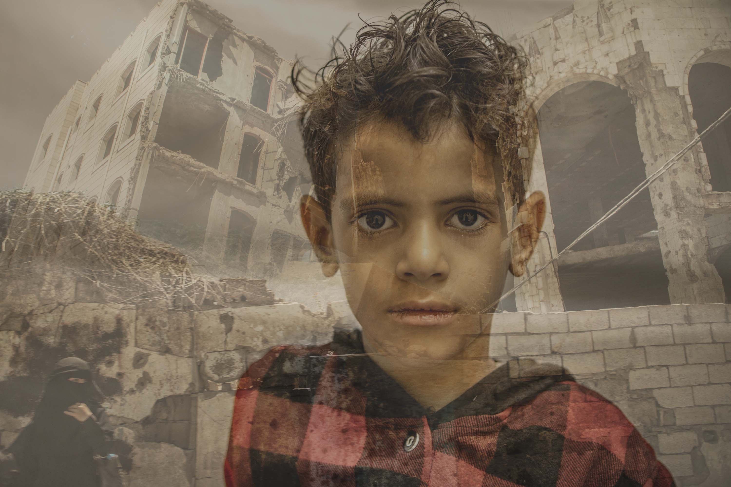 Yemen, 8-year-old boy stands in front of shelled-out buildings