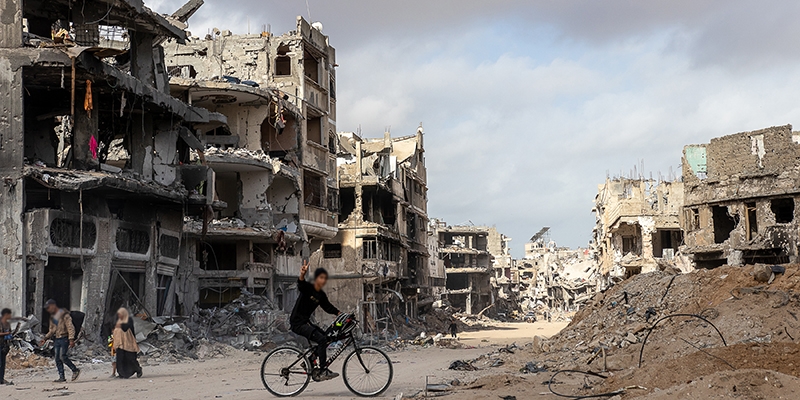 Gaza, a child rides a bike in front of  destroyed buildings in the Gaza strip.