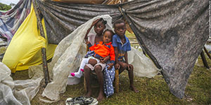 Three boys from Haiti sit in front of a tent. 