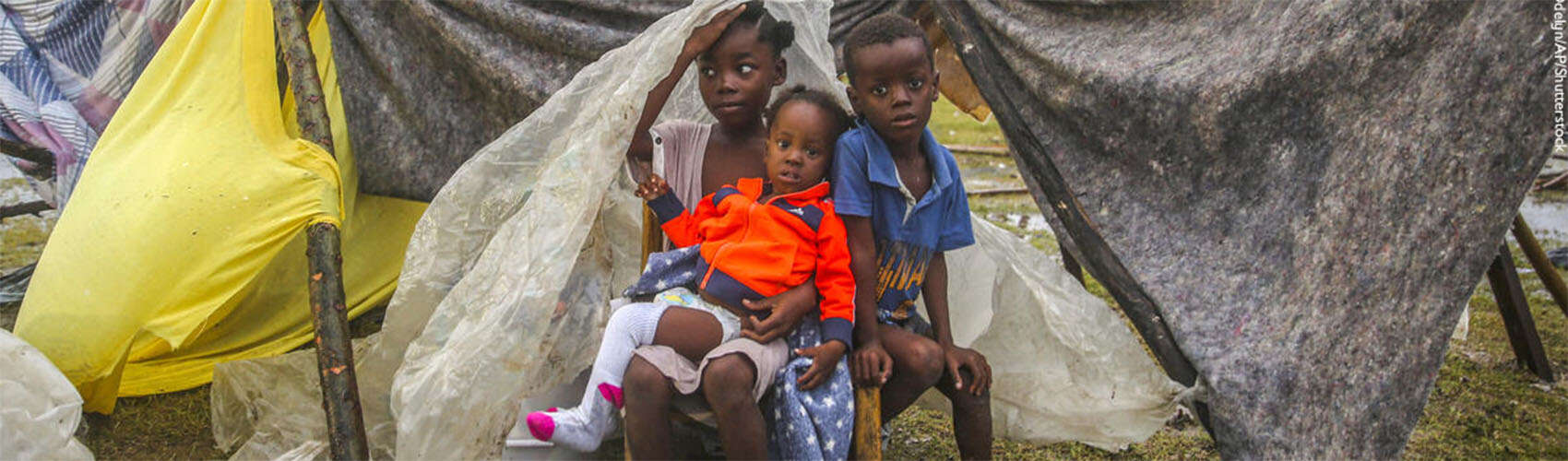Three boys from Haiti sit in front of a tent. 