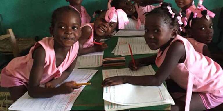 Girls sit at a school desk in their classroom in Haiti. 