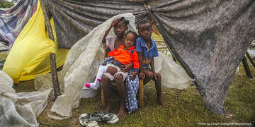 Three young children sit together outside a damaged building in Haiti following a devastating earthquake.