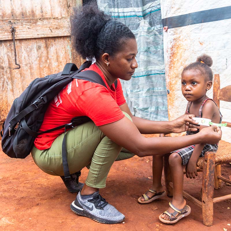 In Haiti, a Save the Children staffer kneels while measuring the arm of a child who is being screened for malnutrition. 