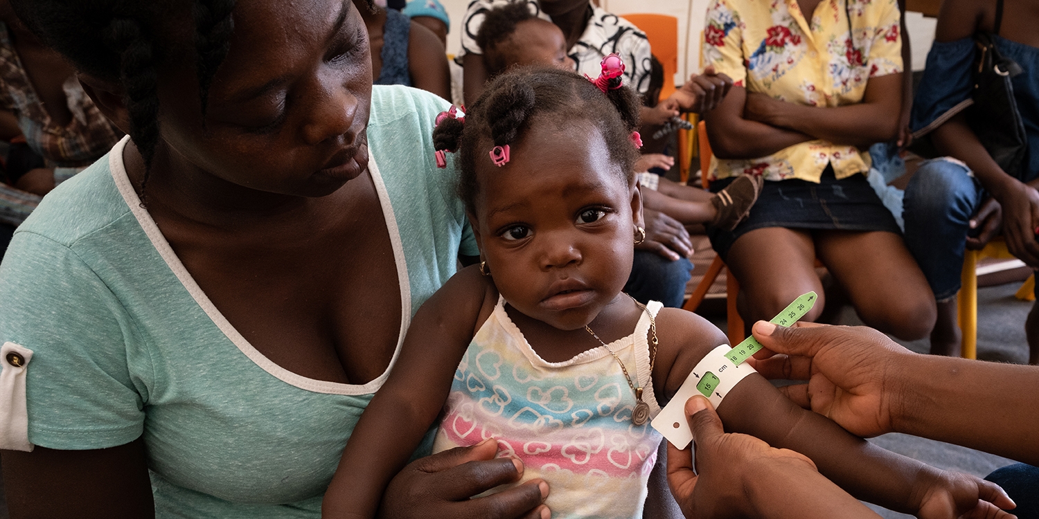 Haiti, a mother holds her small daughter who's arm is being measured for malnutrition