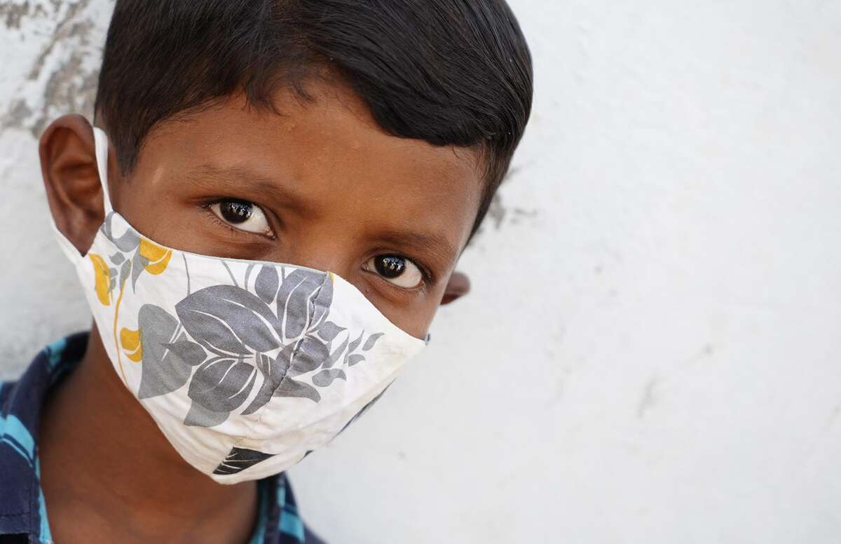 A child from India looks at the camera wearing a mask for COVID-19 prevention